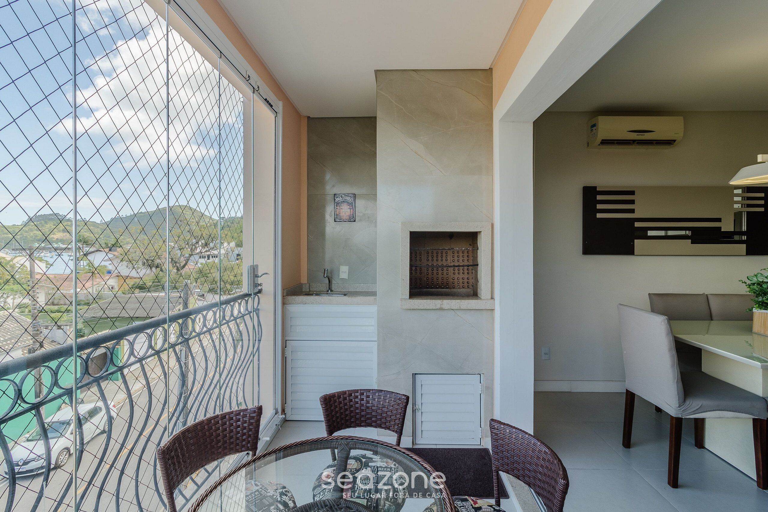 Ein Balkon mit Korbstühlen, einem Glastisch und Blick auf eine Straße und Hügel.