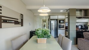 A modern kitchen with a built-in oven, microwave, and refrigerator. There is a dining table with chairs and a potted plant. - Apt w/ BBQ & View, 130m From Beach Rsd0202 (Porto Belo)