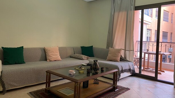 Ein Wohnzimmer mit einer Couch, einem Glastisch und Blick durch eine Glastür auf einen Balkon.