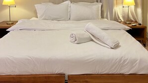 Ein ordentlich bezogenes Bett mit weißen Leinen, zwei Nachttischlampen und einem hölzernen Kopfteil.
