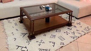 Ein Wohnzimmer mit einem Glastisch, einem weißen Sofa mit Kissen und einem gemusterten Teppich.