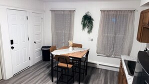 Een compacte keuken met een houten tafel, stoelen, een spoelbak en een afvalbak.