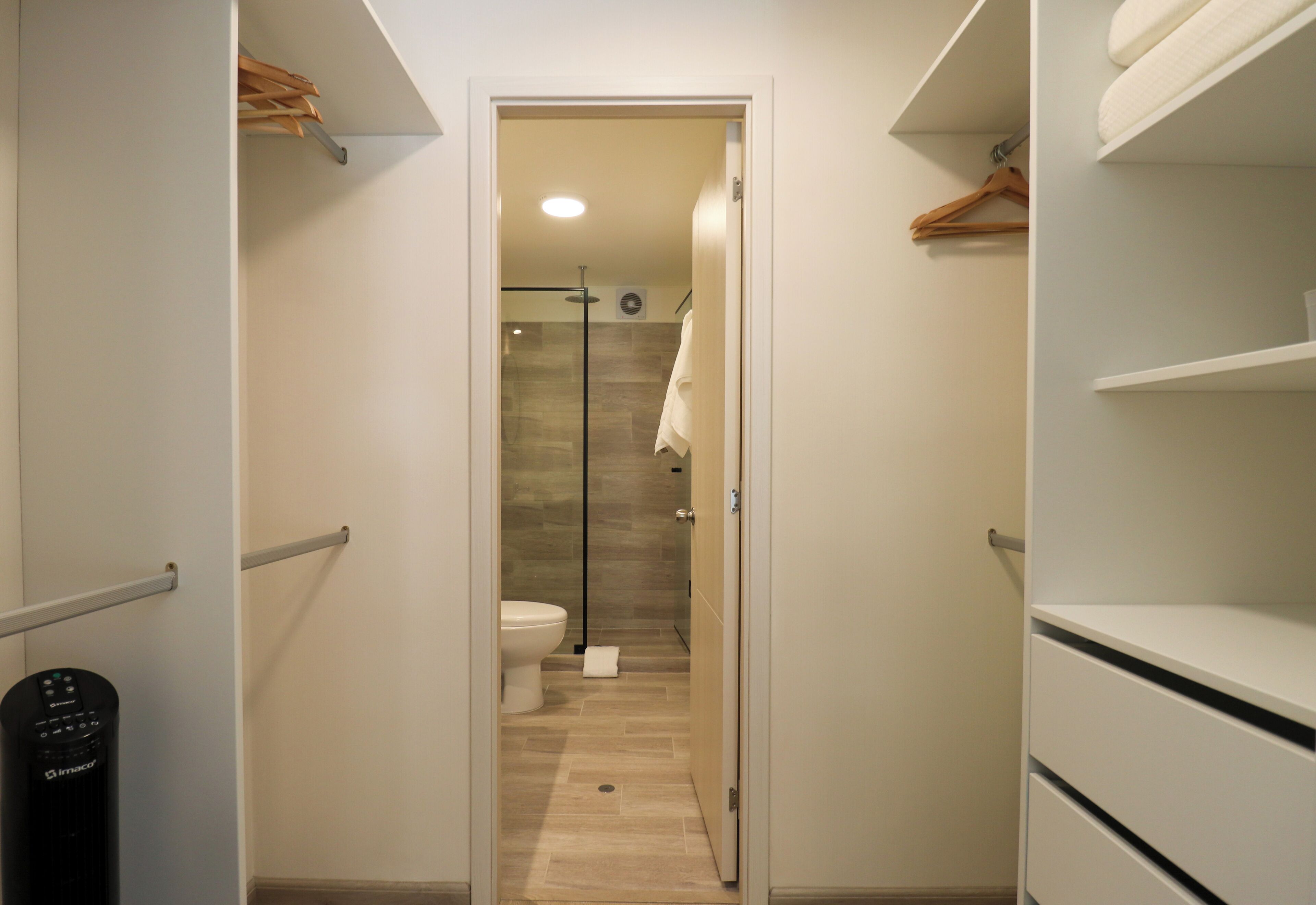 Een smalle gang die leidt naar een badkamer met toilet, douche en een handdoek aan de muur.