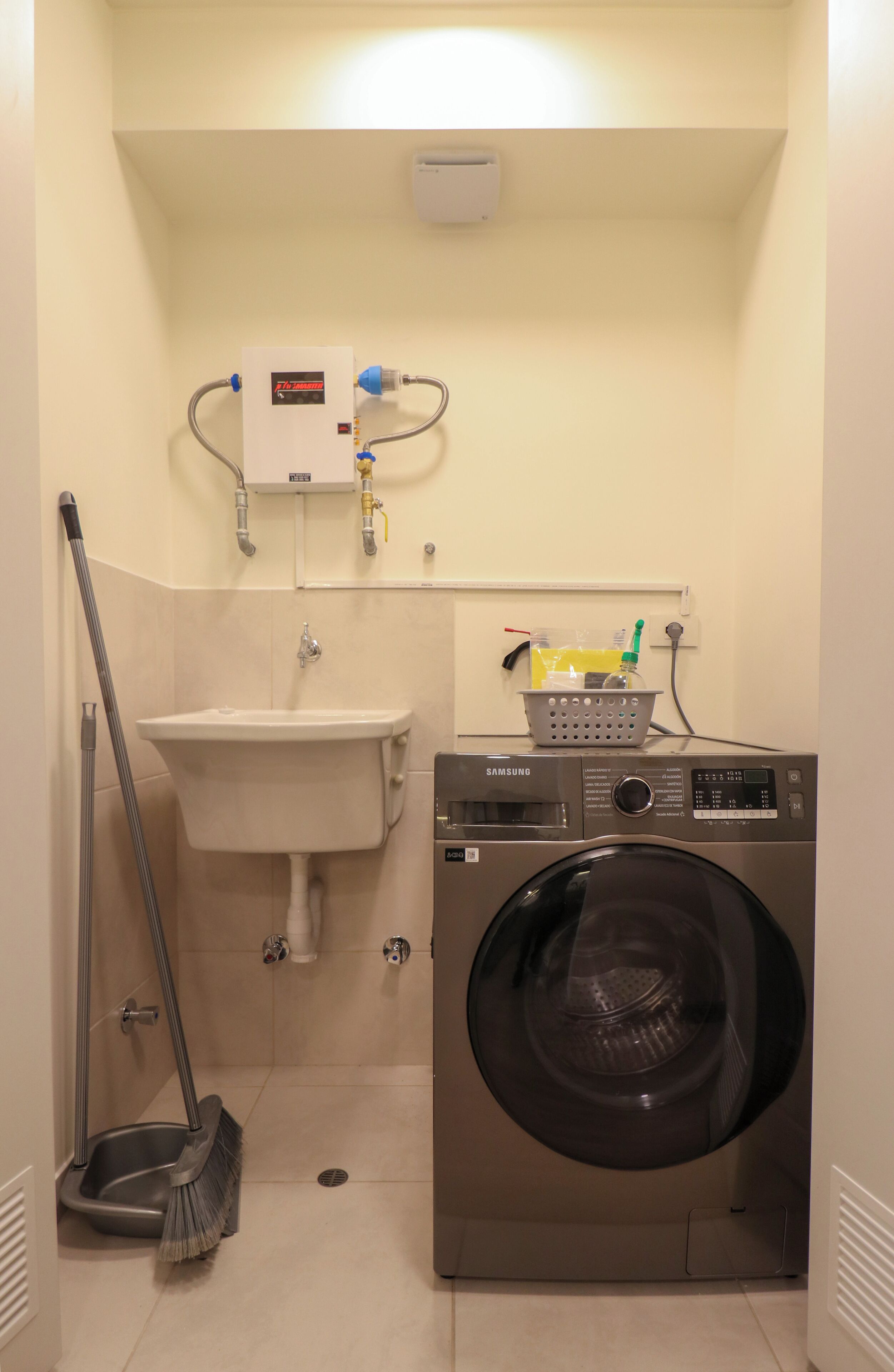 A compact bathroom with a sink, a washing machine, and a mop.
