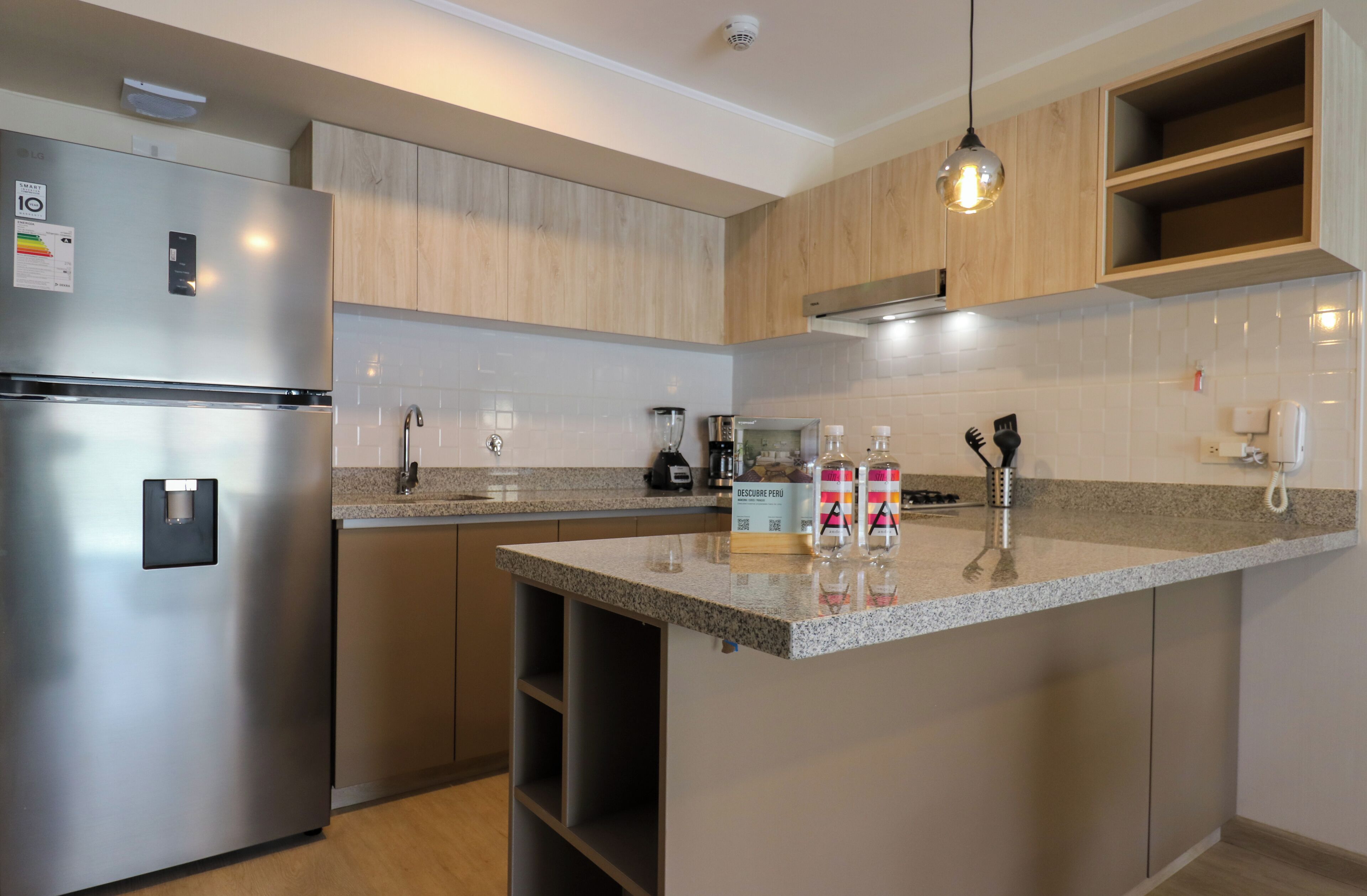 A modern kitchen with a stainless steel refrigerator, wooden cabinets, a granite countertop, and a built-in island.
