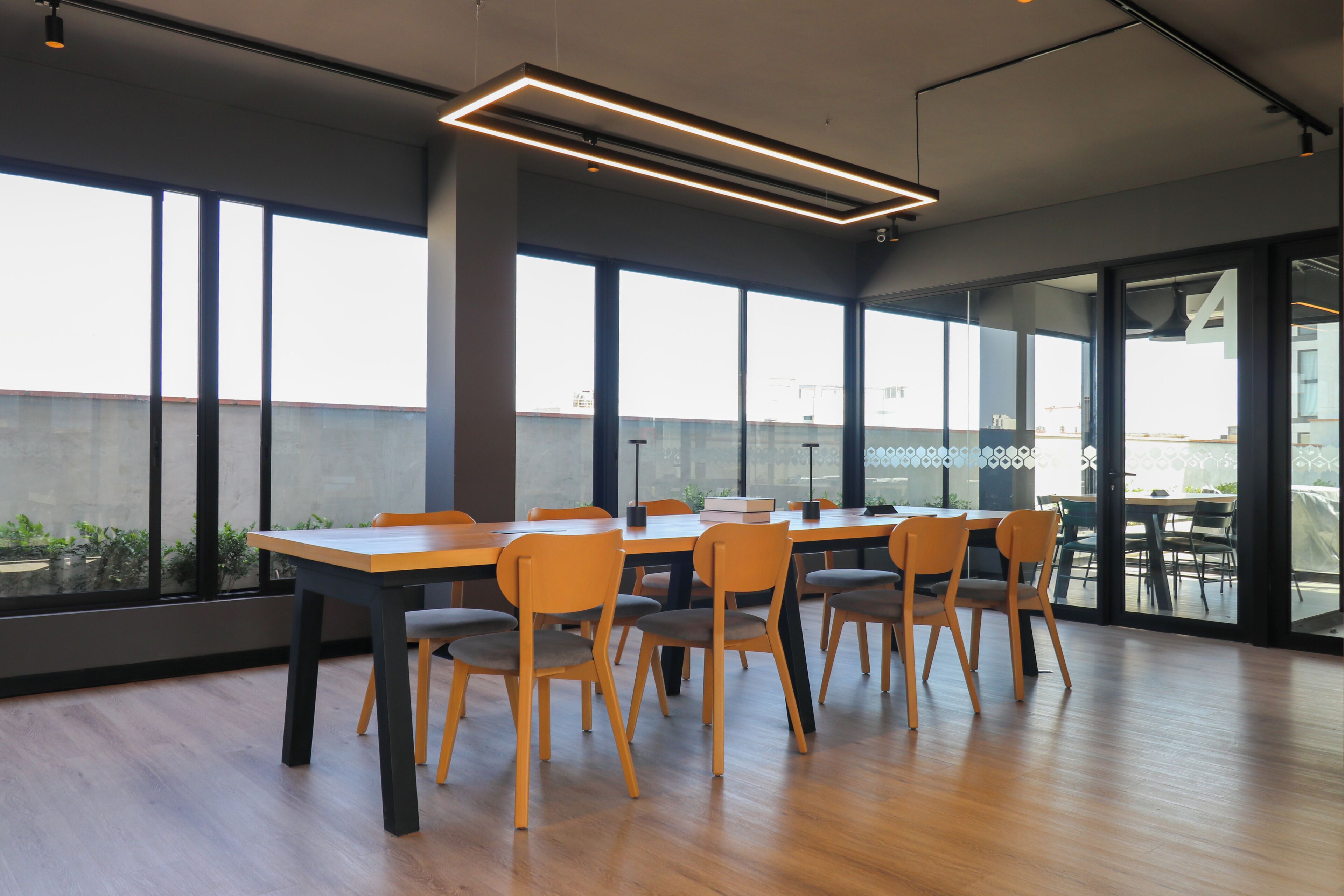 Uma sala de conferências moderna com uma mesa comprida, várias cadeiras, janelas amplas e vista para o exterior.