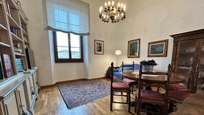 Una zona de menjador amb taula de fusta, cadires, un candelabrum, una catifa amb dibuixos i una prestatgeria.
