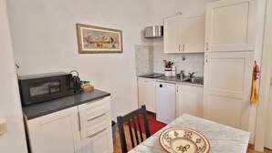 Una cuina compacta amb armaris blancs, taulell negre, microones, rentapelats i una taula de dinar petita.
