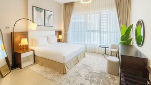 A hotel room with a bed, bedside lamps, a small round table, a chair, a potted plant, and a mirror. - Luxury 1BR Apartment Near Wolrd Trade Center ALK4 (Dubai)