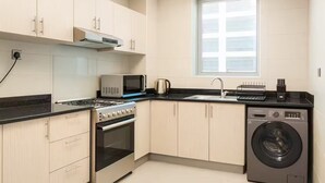 A modern kitchen with light wood cabinets, a stainless steel stove, a microwave, a sink, and a washing machine. - Luxury 1BR Apartment Near Wolrd Trade Center ALK4 (Dubai)