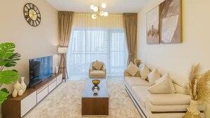 A modern living room with a flat-screen TV, a coffee table, a sofa, a chair, and a large window with sheer curtains. - Luxury 1BR Apartment Near Wolrd Trade Center ALK4 (Dubai)