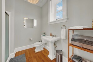 A bathroom with a toilet, sink, mirror, and a towel rack with towels. - Huge 1st floor Historic Apartment Soaring Ceilings (Wilmington)