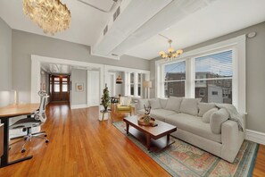 A spacious living room with hardwood flooring, a large sofa, a dining area with a table and chairs, and a kitchen in the background. - Huge 1st floor Historic Apartment Soaring Ceilings (Wilmington)