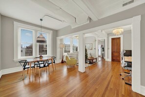 A spacious living area with hardwood flooring, a dining table with chairs, a chandelier, and a view through large windows. - Huge 1st floor Historic Apartment Soaring Ceilings (Wilmington)