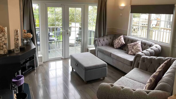 Ein großzügiges Wohnzimmer mit grauem Sofa, Ottoman und Kamin. Eine Glastür öffnet sich zu einer Außenpatiofläche.