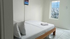 A single-bed room with a wooden frame, white bedding, a small painting on the wall, and a window with a view of a snowy landscape. - Hotel O 95063 Afifah Syariah Guest House Manado (Manado)