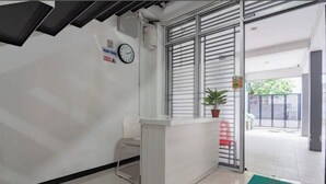 A reception area with a white counter, a clock, and a potted plant. - Hotel O 95063 Afifah Syariah Guest House Manado (Manado)