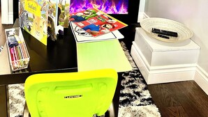 A flat-screen TV mounted on a wall displaying a streaming app interface. Below the TV, there are children's books and a bright yellow chair. - Family style cozy living in friendly surroundings (Ajax)