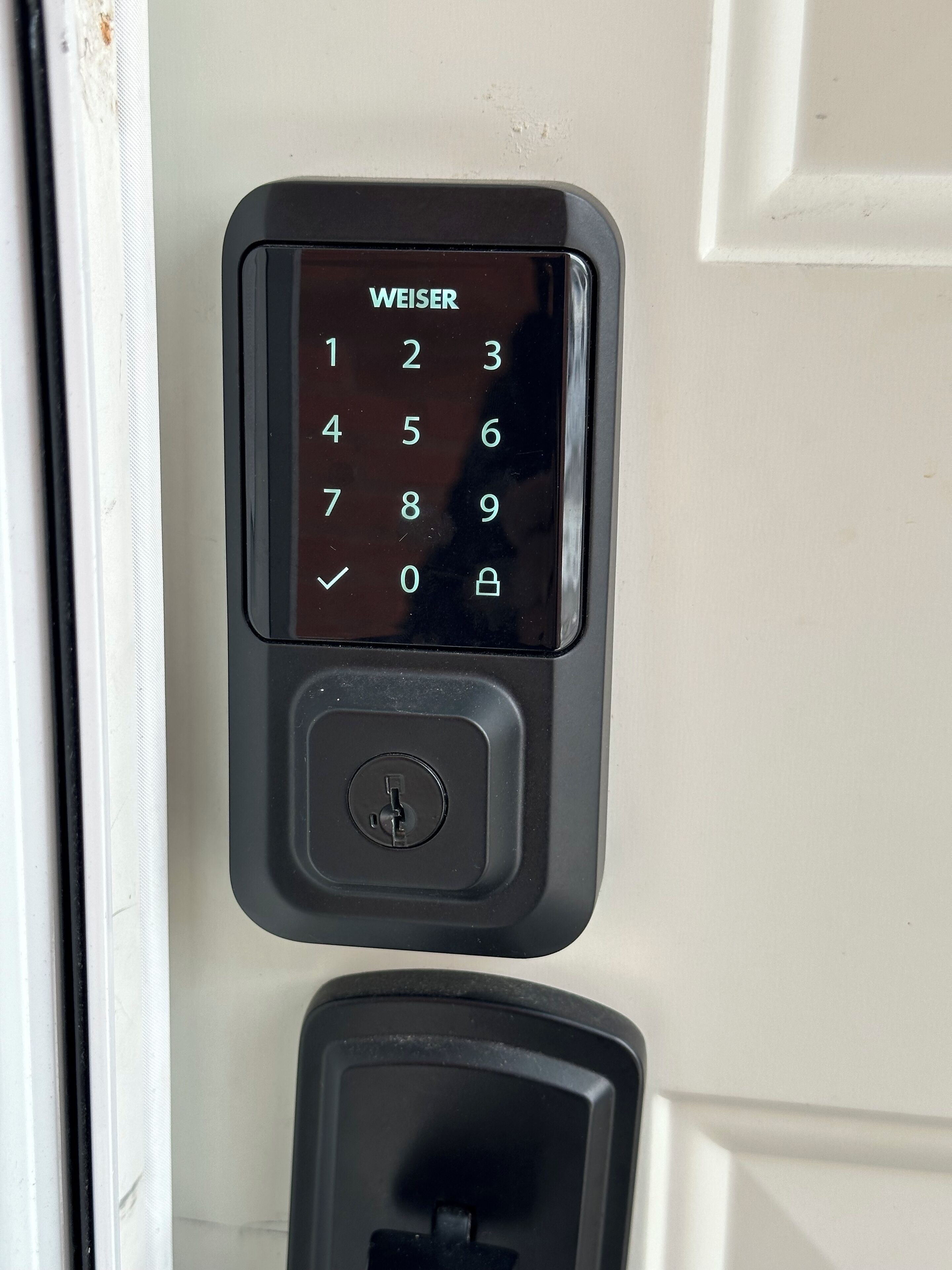 Un teclado numérico negro con un botón de bloqueo y una cerradura debajo, montado en una puerta blanca.