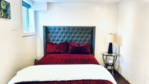 A modern bedroom with a large bed, a tufted headboard, a glass side table, and a patterned rug. - Family style cozy living in friendly surroundings (Ajax)