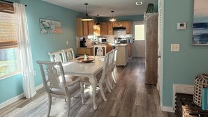 Un comedor amplio con una mesa y sillas de madera, una cocina al fondo y vistas al exterior a través de una ventana.