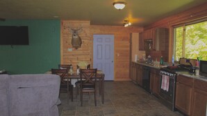 A cozy cabin interior with a dining area, kitchen, and a mounted deer head on the wall. - Twisted House (Arkansaw)