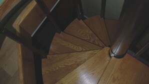 A wooden spiral staircase with a black metal handrail, a wooden floor, and a light green wall. - Twisted House (Arkansaw)