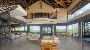 Un salón espacioso con pared de piedra, escalera de madera y un amplio ventanal con vistas al exterior.