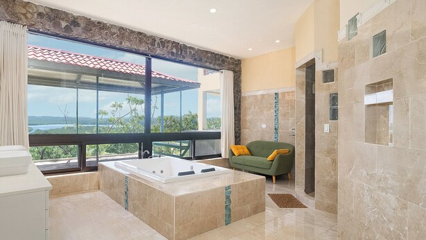 Un baño moderno con una bañera grande, un sofá verde y vistas a un paisaje natural.