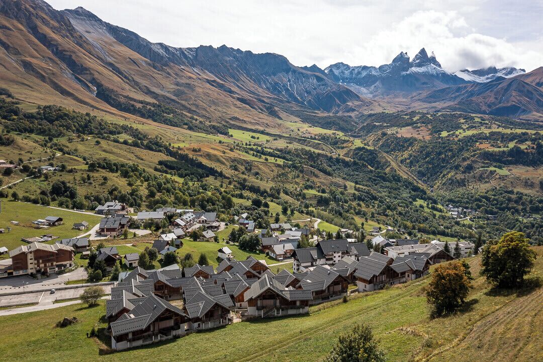 Un grupo de edificios tradicionales de madera con techos inclinados, probablemente un pueblo de montaña con un valle y montañas al fondo.
