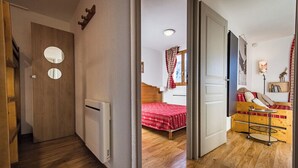 A hallway leading to a bedroom with a wooden floor, a radiator, a bed with a red bedspread, and a small table with a lamp. - Apartment for 4 - 6 people in Albiez-Montrond (Albiez-Montrond)
