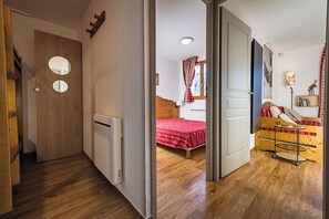 A hallway leading to a bedroom with a wooden floor, a radiator, a bed with a red bedspread, and a small table with a lamp. - Apartment for 4 - 6 people in Albiez-Montrond (Albiez-Montrond)