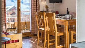 A dining area with wooden chairs and a table, a television mounted on the wall, and a view of mountains through a glass door. - Apartment for 4 - 6 people in Albiez-Montrond (Albiez-Montrond)