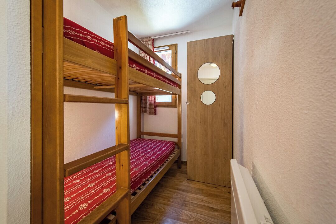 A narrow hallway with bunk beds and a wooden door with two circular windows.