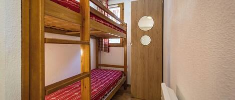 A narrow hallway with bunk beds and a wooden door with two circular windows.