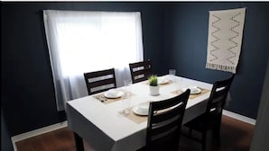 Un coin repas avec une table dressée pour quatre personnes, comprenant des assiettes, des verres et une petite plante.