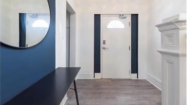 Un couloir avec une console noire, un grand miroir et une porte blanche dotée d’un cadre noir.