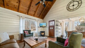 Una sala de estar acogedora con techo de madera, chimenea, televisor y puerta para huéspedes.