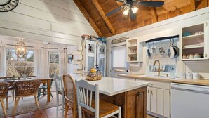 Una cocina con techo de madera, armarios blancos y una zona de comedor con sillas de mimbre.