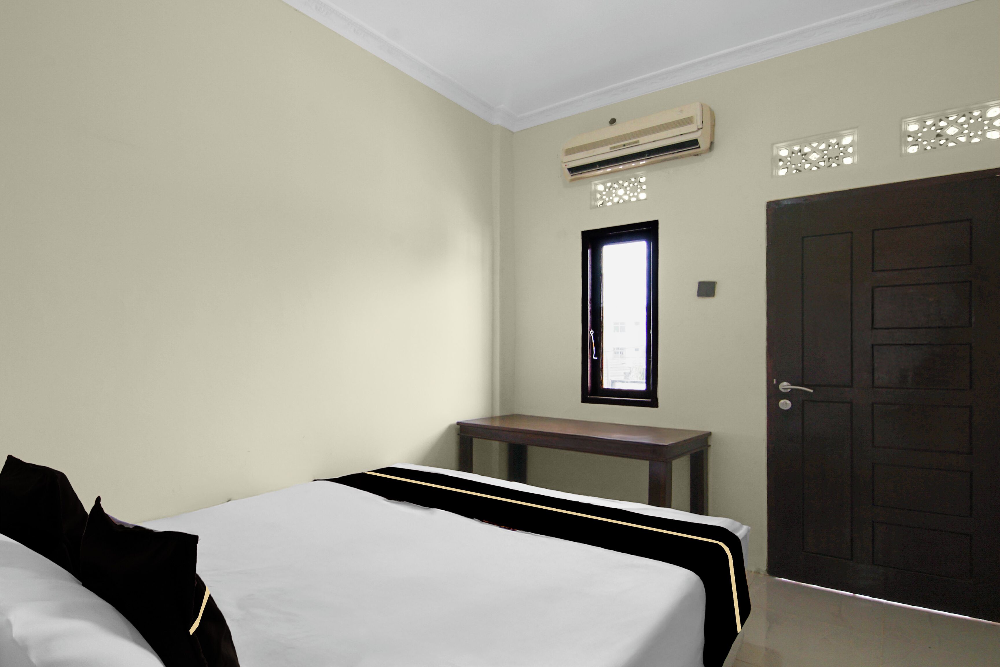 Ein Hotelzimmer mit Bett, kleinem Tisch, Tür und Klimaanlage.