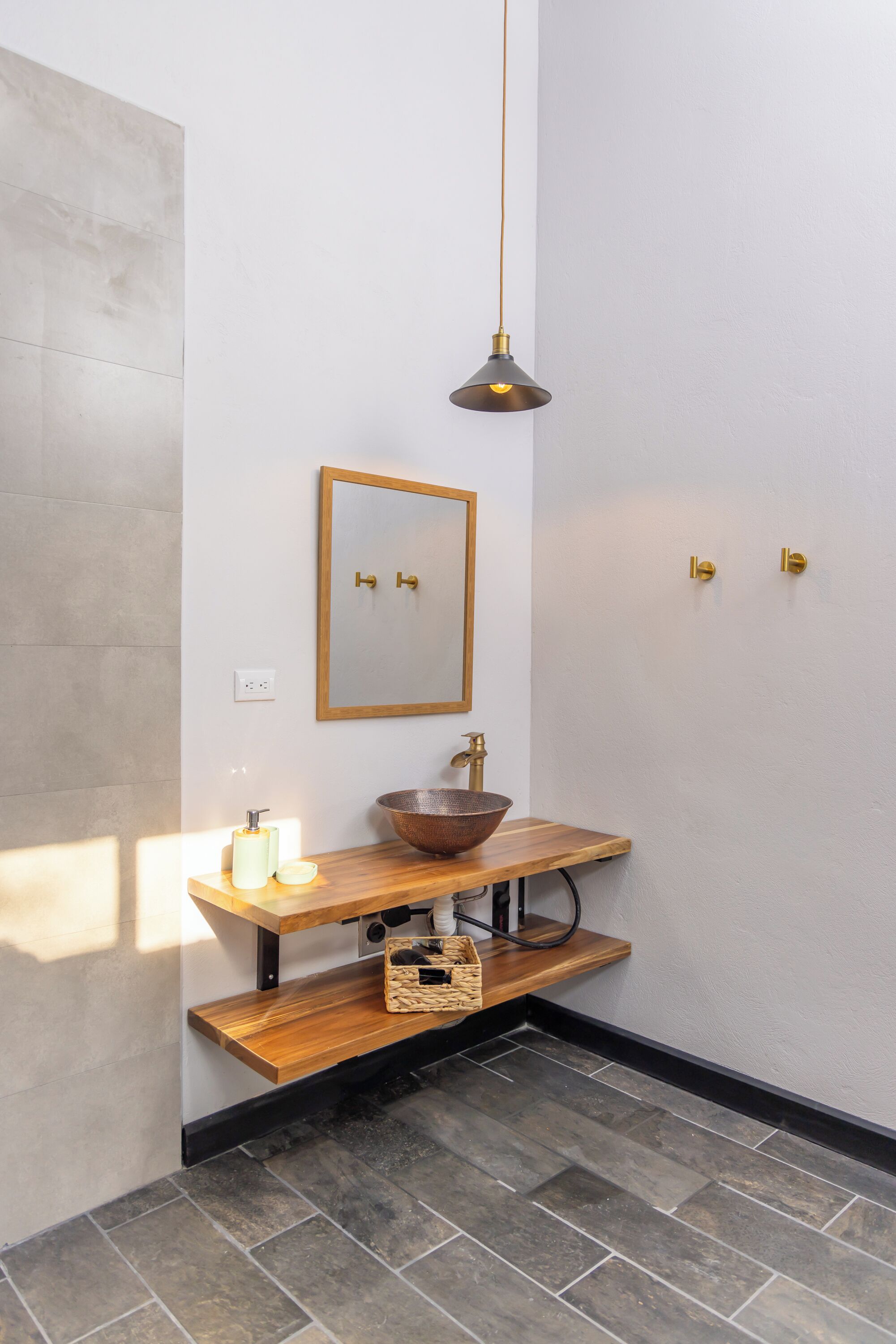 A bathroom with a wooden vanity, a copper sink, a mirror, and a pendant light.