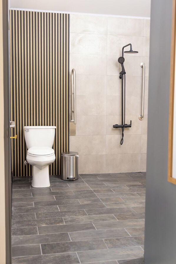 A modern bathroom with a toilet, a shower, and a trash bin.