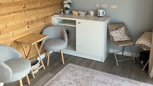 Een gezellige kamer met een houten plafond, een wit bureau, twee grijze stoelen en een kamerkleed met dessin.