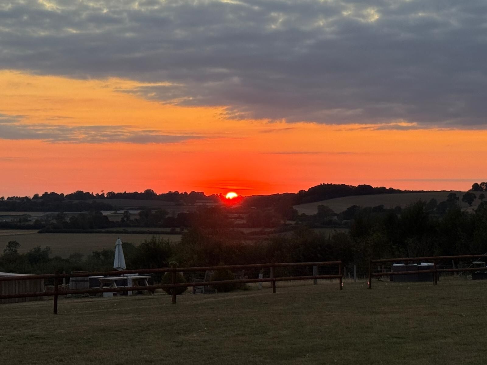 Un coucher de soleil sur un paysage rural, avec des champs et une clôture.
