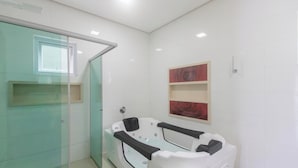 A modern bathroom with a glass shower enclosure, a white bathtub with black seats, and a wall-mounted rose decoration. - House w/ Pool and Barbecue Grill Thg0006 (Porto Seguro)