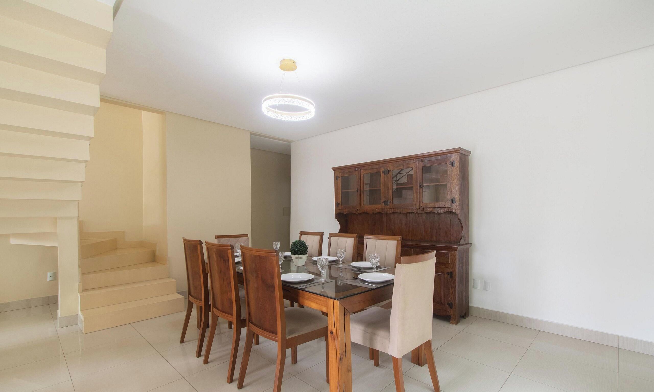 A dining area with a table set for four, wooden chairs, a cabinet with glass doors, and a staircase leading to another level.