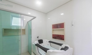 Een moderne badkamer met een glazen douchecabine, een witte badkuip met zwarte zitjes, en twee rode rozen schilderijen aan de muur.