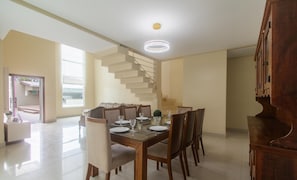 Een eetgedeelte met een houten tafel voor vier personen, omringd door stoelen. Achtergrond toont een wenteltrap die naar een hoger niveau leidt.