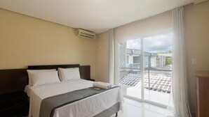 A hotel room with a bed, a bedside table, a window with a view of the outside, and an air conditioning unit on the wall. - House w/ Pool and Barbecue Grill Thg0006 (Porto Seguro)