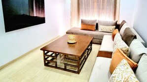 Un salon moderne avec une table basse en bois, un ensemble de canapés et un grand téléviseur à écran plat fixé au mur.